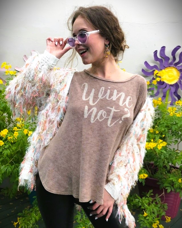 Miriam smiling and wearing sunglasses, standing near a bush with yellow flowers.